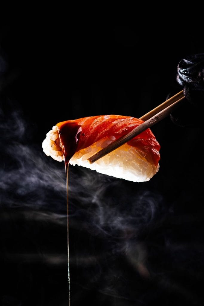Sushi-etiquette in Japan: dit moet je weten – Kitsune Travel Sushi-etiquette in Japan: close-up van nigiri met druipende sojasaus, tegen een rokerige zwarte achtergrond.