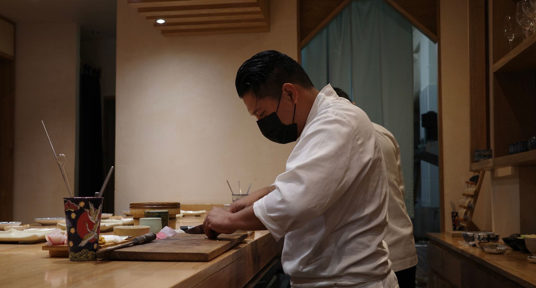 Sushi-etiquette in Japan: dit moet je weten – Kitsune Travel Een sushichef snijdt met grote precisie vis in een gezellig Japans restaurant en demonstreert daarbij zijn messentechniek.
