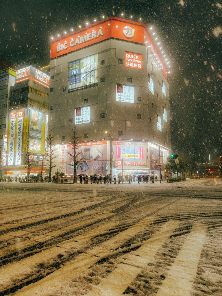 Een verlichte straat in Tokio 's nachts, met vallende sneeuw, die het stadsleven en de winterse charme vastlegt.