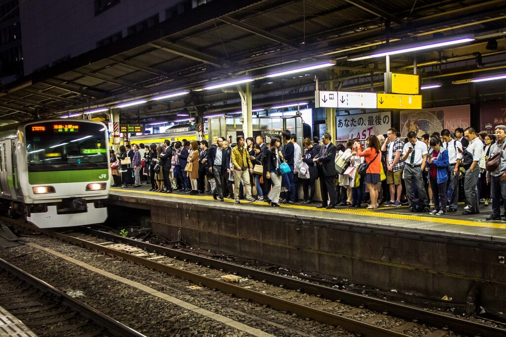 Openbaar vervoer in Tokyo: zo werkt het, van metro tot waterbus – Kitsune Travel Reizigers wachten op het drukke perron van de Yamanote-lijn in Shinjuku terwijl een trein binnenrijdt