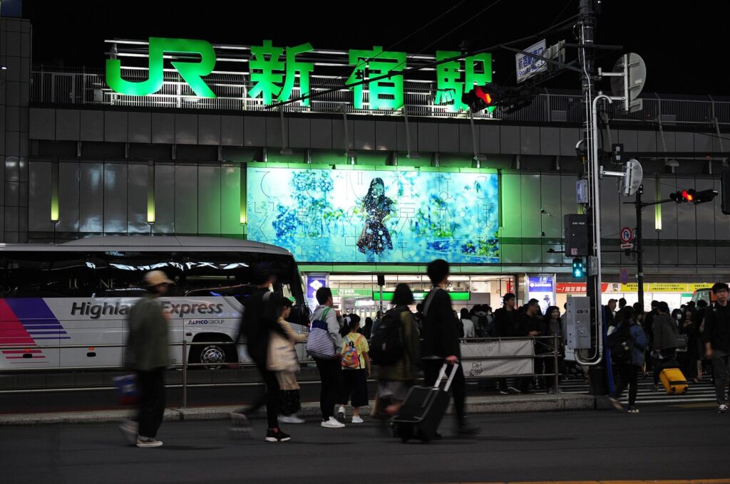Groen bord van Shinjuku Station in de avond met reizigers en koffers