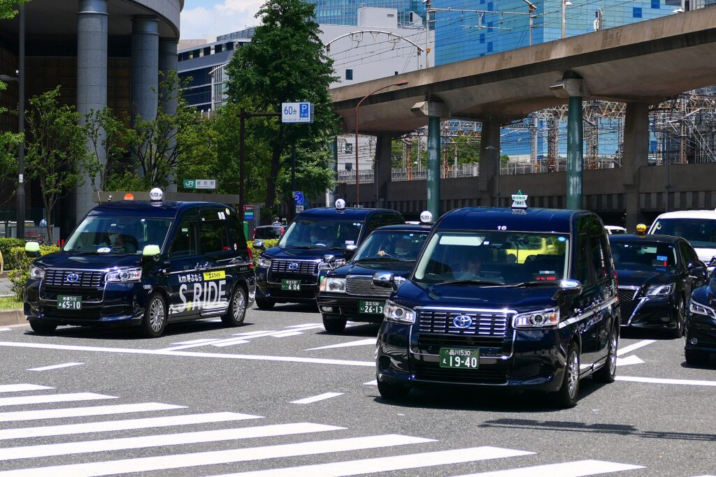 Openbaar vervoer in Tokyo: zo werkt het, van metro tot waterbus – Kitsune Travel Een rij donkerblauwe taxi's op een kruispunt in Marunouchi, Tokyo